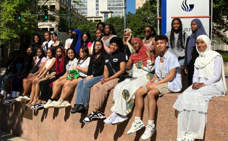 A group of students sit on a wall, posing for a picture during a college tour.